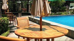 A poolside area with wooden tables and chairs, a pool, and surrounding greenery. - Studio Apartment at Taguig Manila (Taguig)