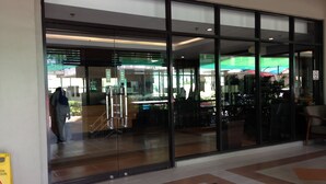 A modern building entrance with glass doors, a tiled floor, and a visible outdoor seating area with umbrellas. - Studio Apartment at Taguig Manila (Taguig)