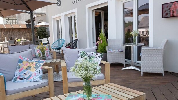 Un área de estar al aire libre con mesas y sillas de madera, un florero con flores y un cartel que dice 'Café Resto Hotel'.