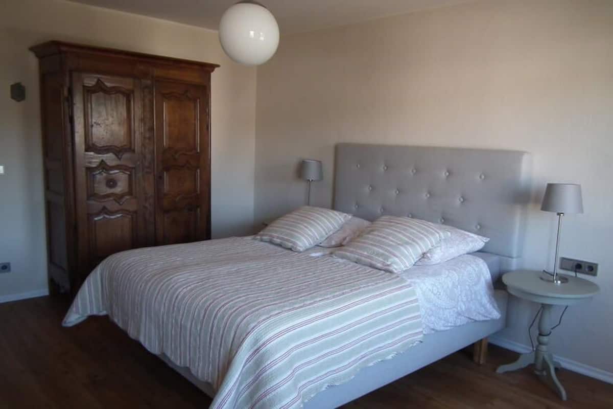 A bedroom with a large bed, a wardrobe, a bedside table, and a lamp.
