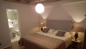 Un dormitorio con una cama grande, dos lámparas de noche, un cabecero y un baño a la vista al fondo.