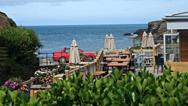 Un espace extérieur aménagé avec des tables et des parasols, situé en bord de mer et offrant une vue sur l’océan.