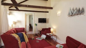 Un salon avec des canapés rouges, un plancher en bois, un téléviseur fixé au mur et un élément décoratif en métal accroché au mur.