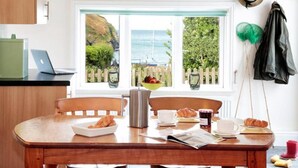 Une table à manger avec des aliments pour le petit-déjeuner, un ordinateur portable et une vue sur la mer par la fenêtre.