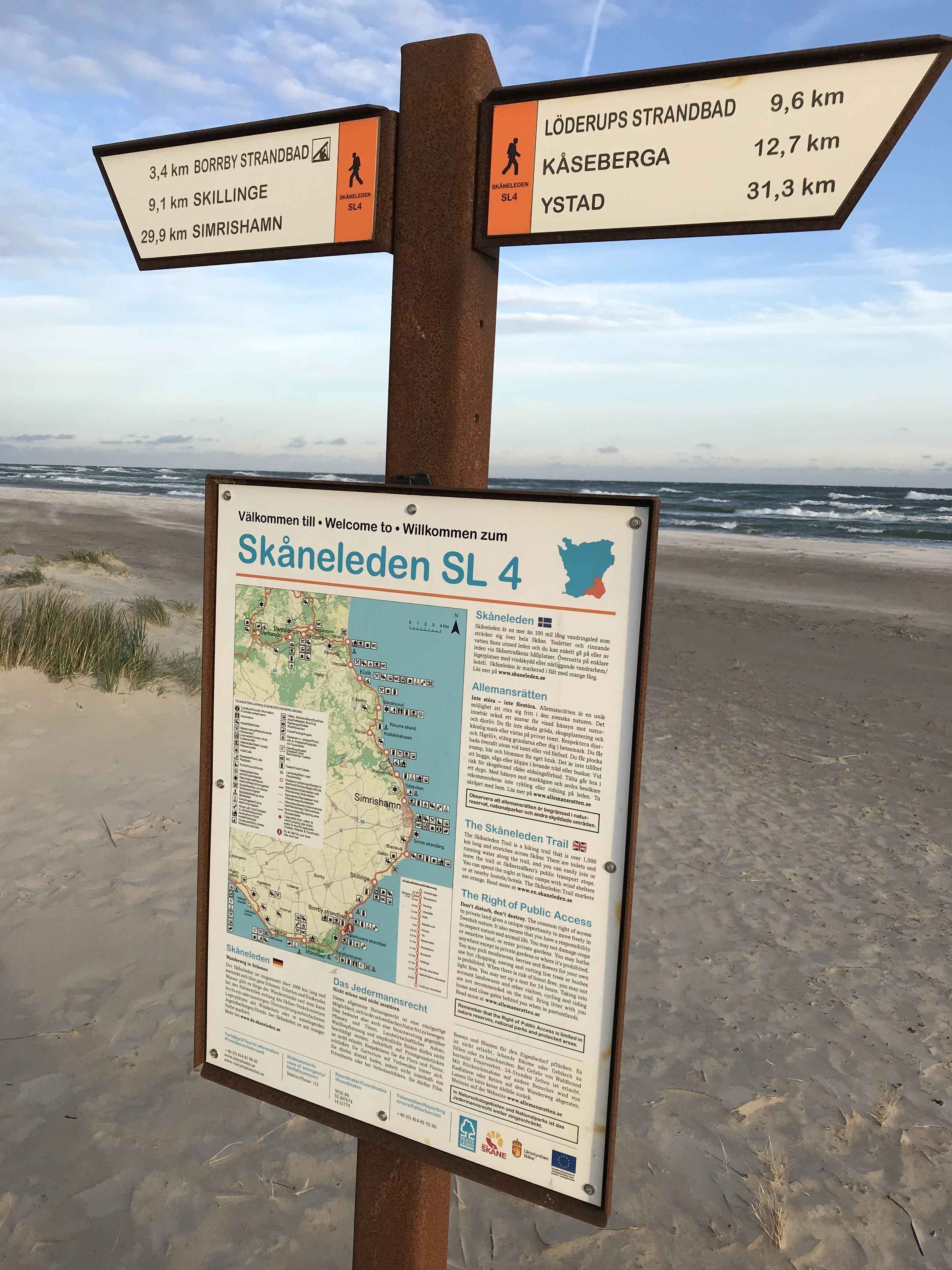 Un cartel con indicaciones y distancias a varios destinos, además de un mapa detallado de la ruta Skåneleden.