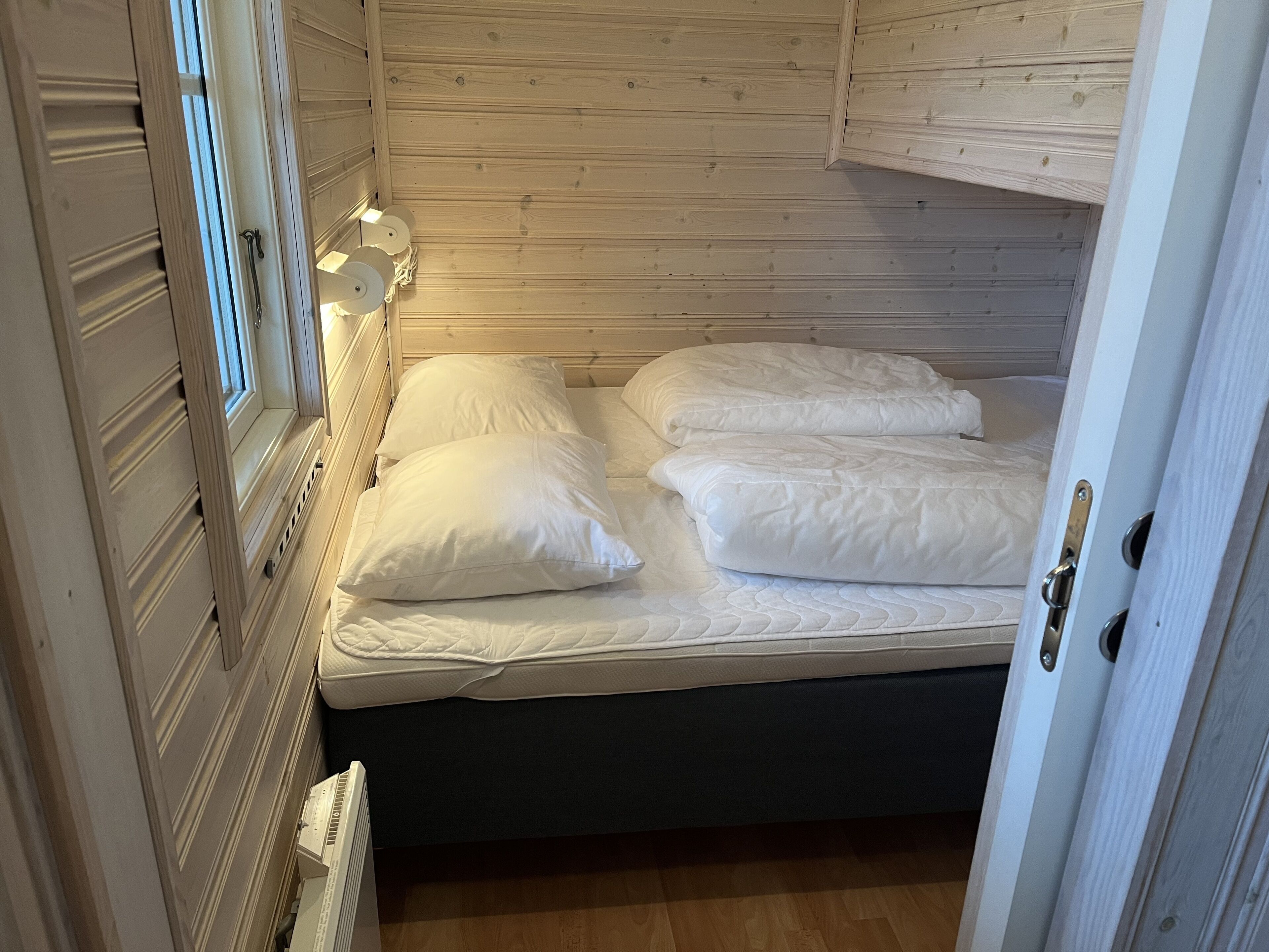 A small, cozy room with a single bed, wooden walls, and a radiator.