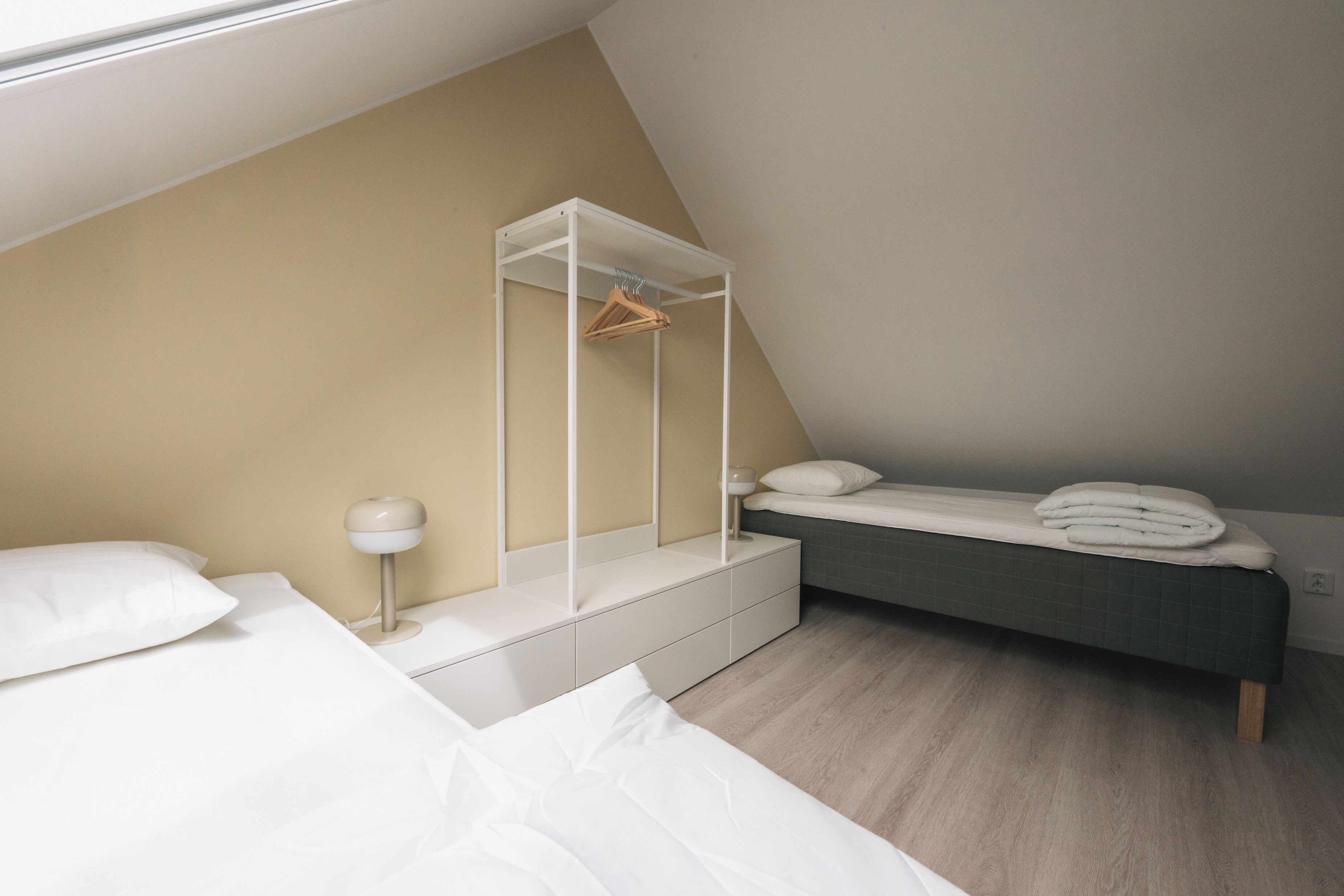 A bedroom with a bed, bedside table, lamp, and a hanging wardrobe.