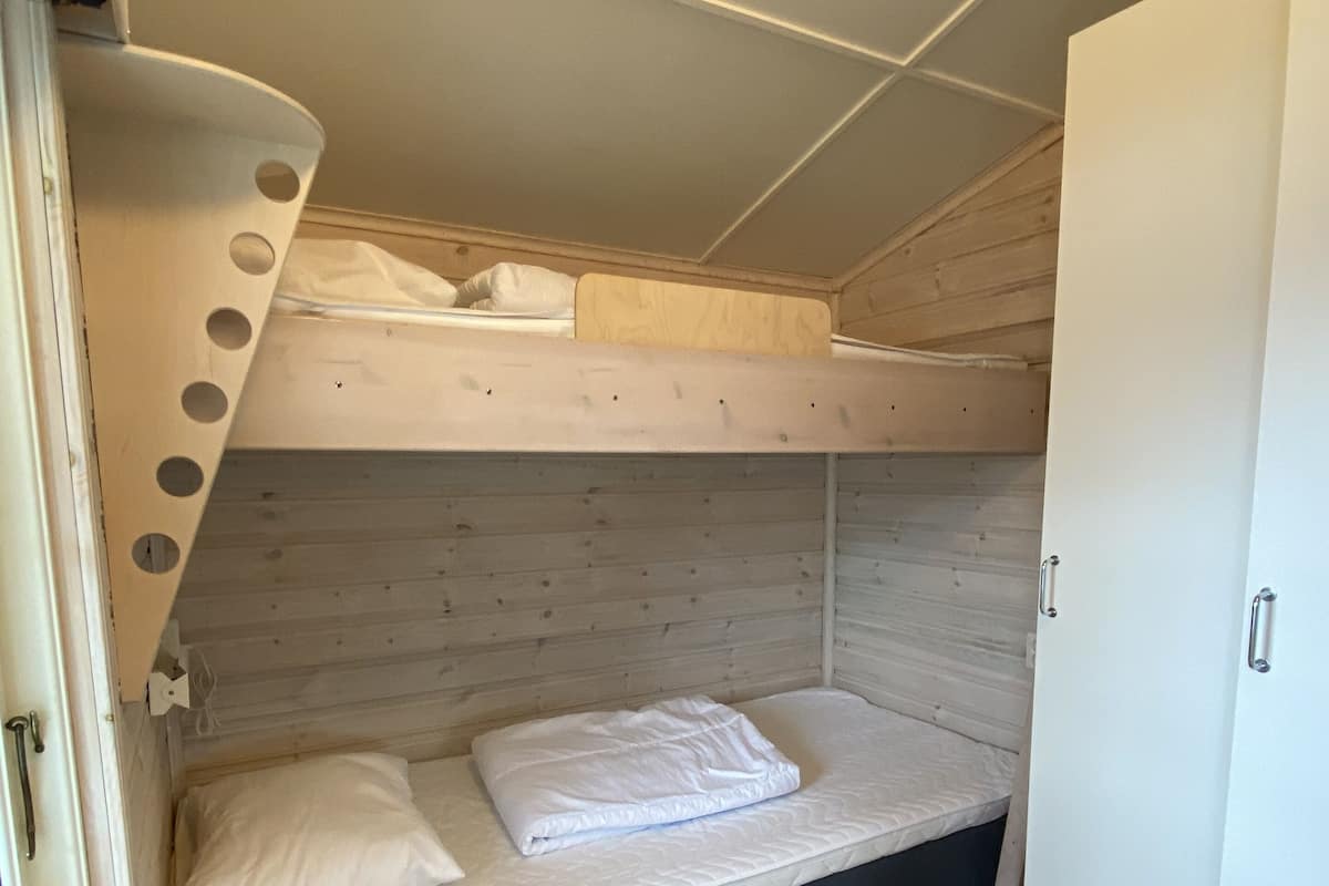 Kerrossängyllä varustettu huone, jossa on puulattia, valkoinen vaatekaappi ja ikkuna, jossa on verhot.