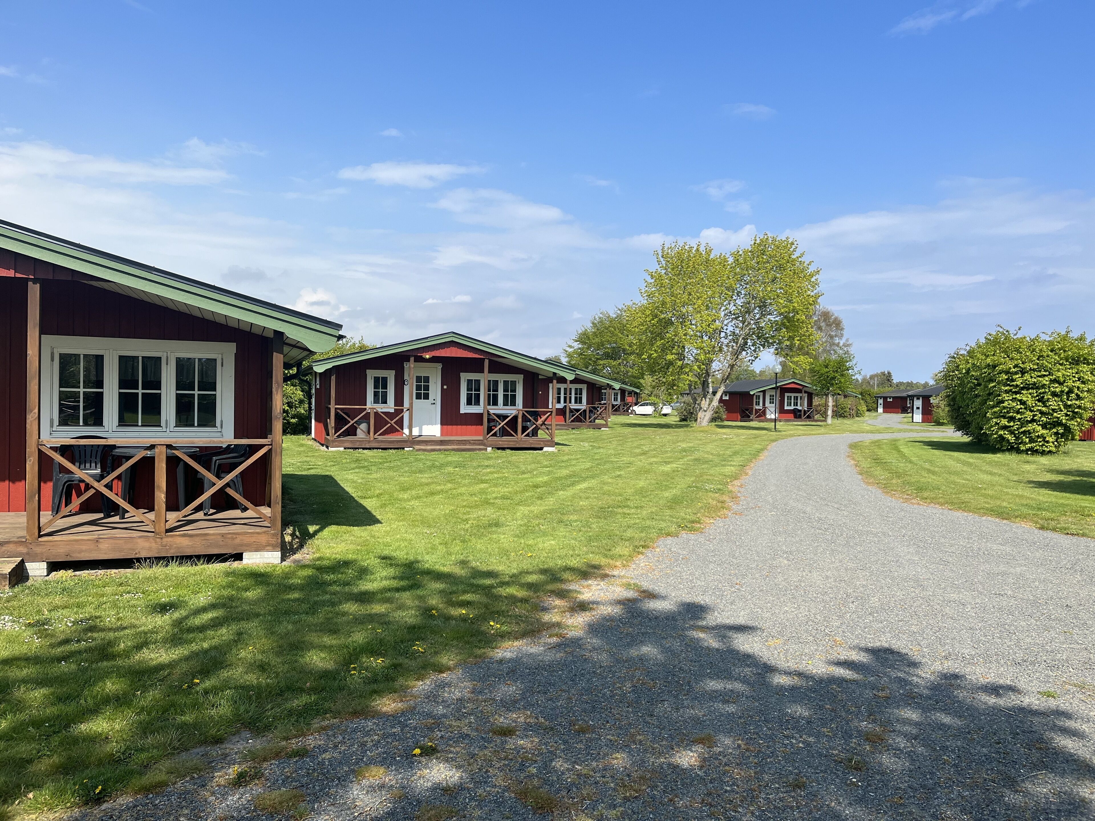 A row of red cabins with a gravel path leading through a grassy area.