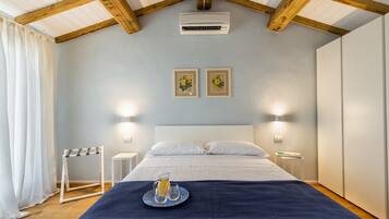 A bedroom with a bed, white curtains, a ceiling fan, two wall-mounted lights, and a small table with a tray of drinks.