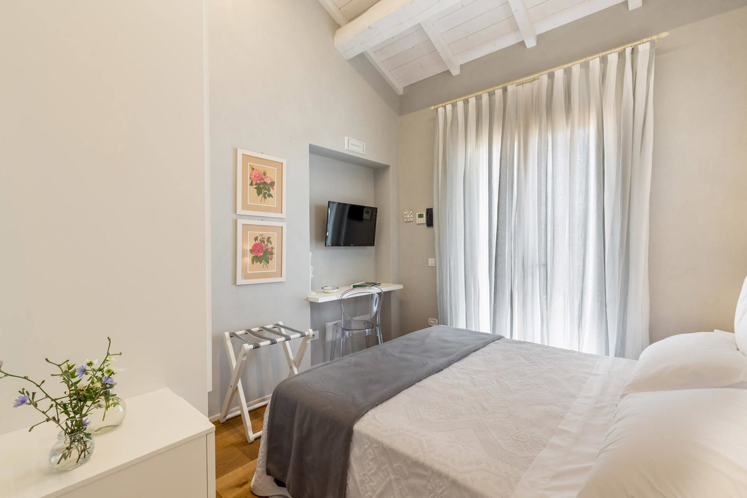 Un dormitorio con cama, escritorio y silla, televisión y ventana con cortinas.