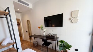 Una habitación de hotel moderna con una cama, un escritorio con silla, un televisor, un espejo grande y una planta en maceta.
