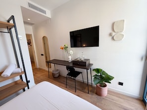 A modern hotel room with a bed, a desk with a chair, a television, a large mirror, and a potted plant. - Casa Vaganto (Barcelona)