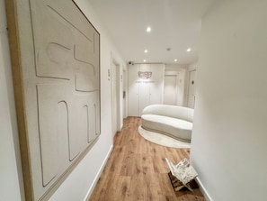 A hallway with a wooden floor, a large abstract wall art piece, and a modern sofa. - Casa Vaganto (Barcelona)