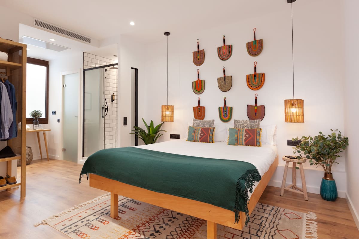 Ein modernes Schlafzimmer mit einem großen Bett, einer Holzbank, einem kleinen Hocker, einer Topfpflanze und einem an der Wand befestigten Regal.