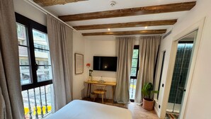 Habitación de hotel con cama, escritorio, televisor y vistas al balcón exterior.
