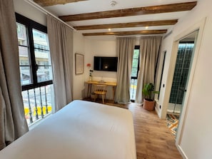 A hotel room with a bed, a desk, a TV, and a view of the outside balcony. - Casa Vaganto (Barcelona)