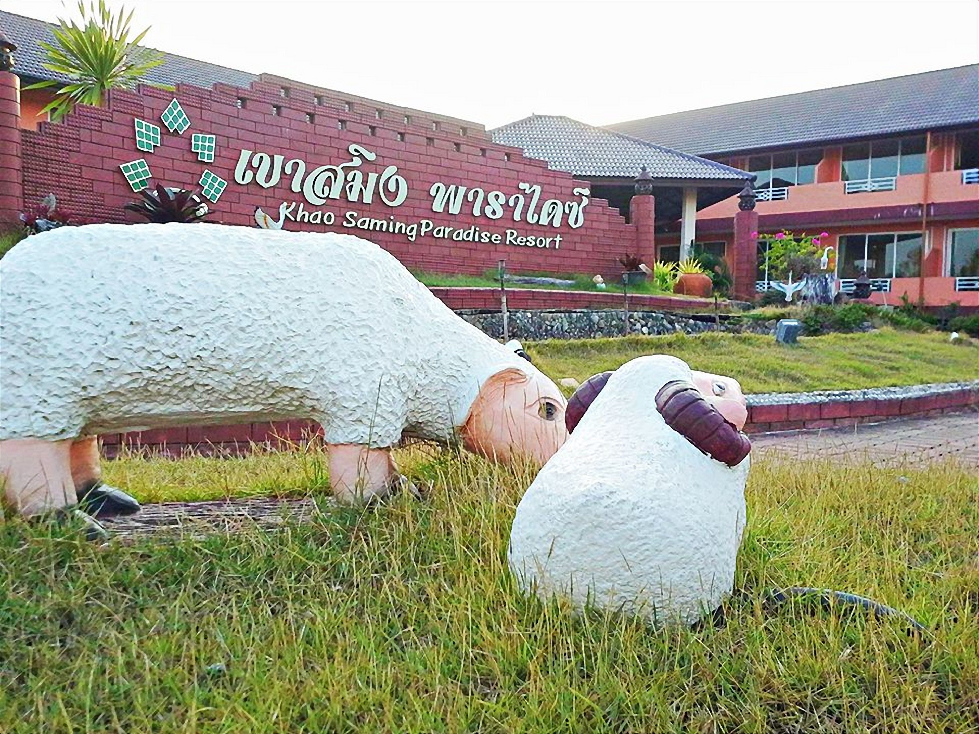 A sign for Khao Saming Paradise Resort with two large, white, sheep-shaped sculptures in front.