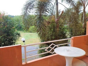 A balcony with a white table and a metal railing overlooking a garden with various trees and a grassy area. - Khao Saming Paradise Resort (Khao Saming)