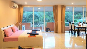 A hotel room with a bed, a dining table, and chairs. There is a balcony with a view of greenery outside. - Khao Saming Paradise Resort (Khao Saming)