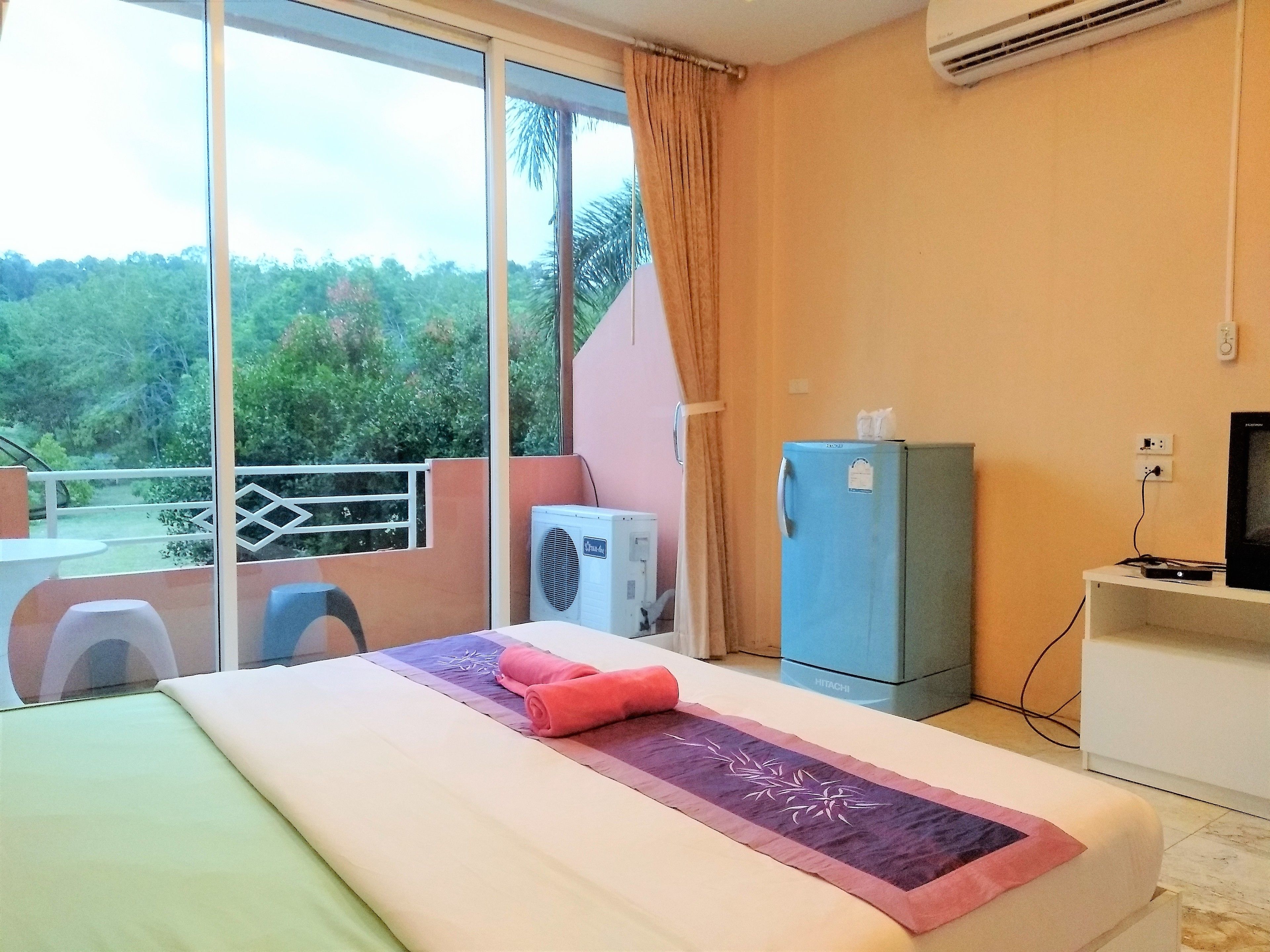 Habitación de hotel con cama, una mesita, una silla, un minibar y televisión.