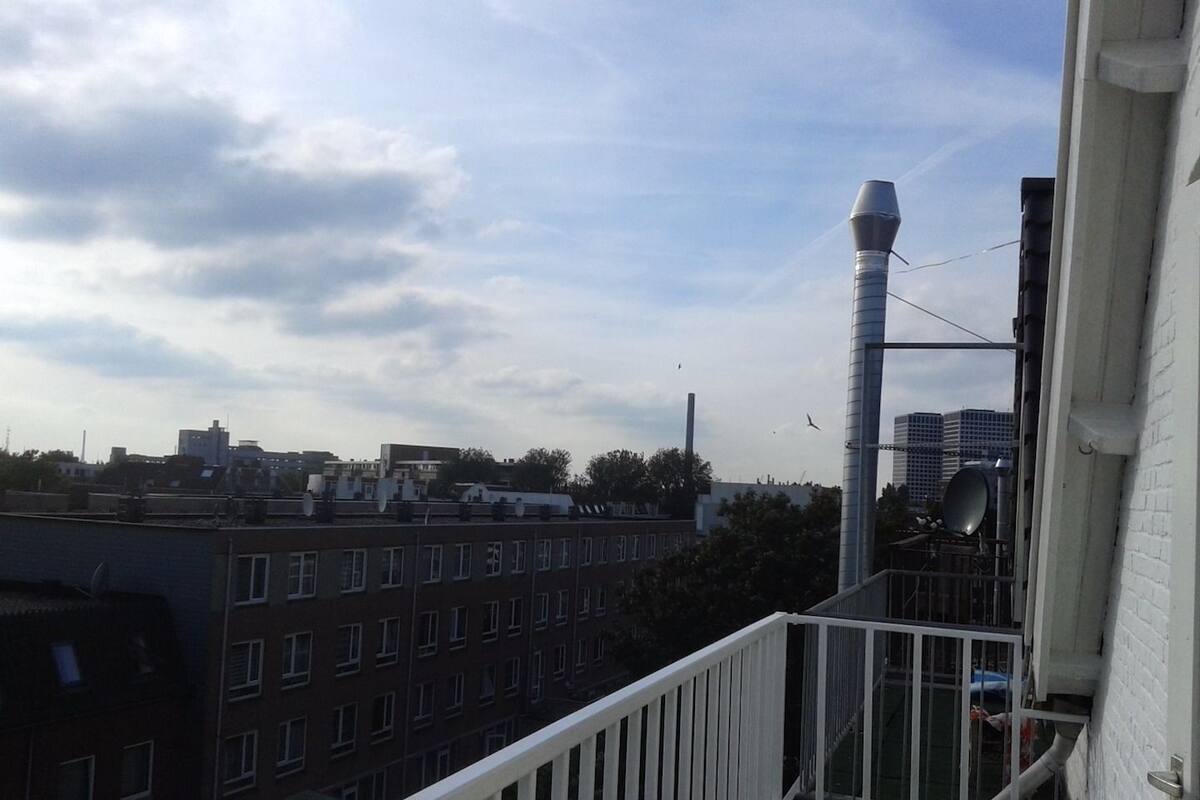 A balcony with a white railing overlooking a cityscape with buildings and a clear sky.