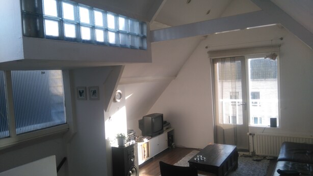 A loft-style room with a sloped ceiling, a TV on a stand, a dining table, and a sofa. - MyCityLofts - Schiedamseweg (Rotterdam)