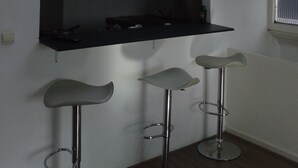 A modern kitchen with a large black countertop, three bar stools, and a wall-mounted TV. - MyCityLofts - Schiedamseweg (Rotterdam)
