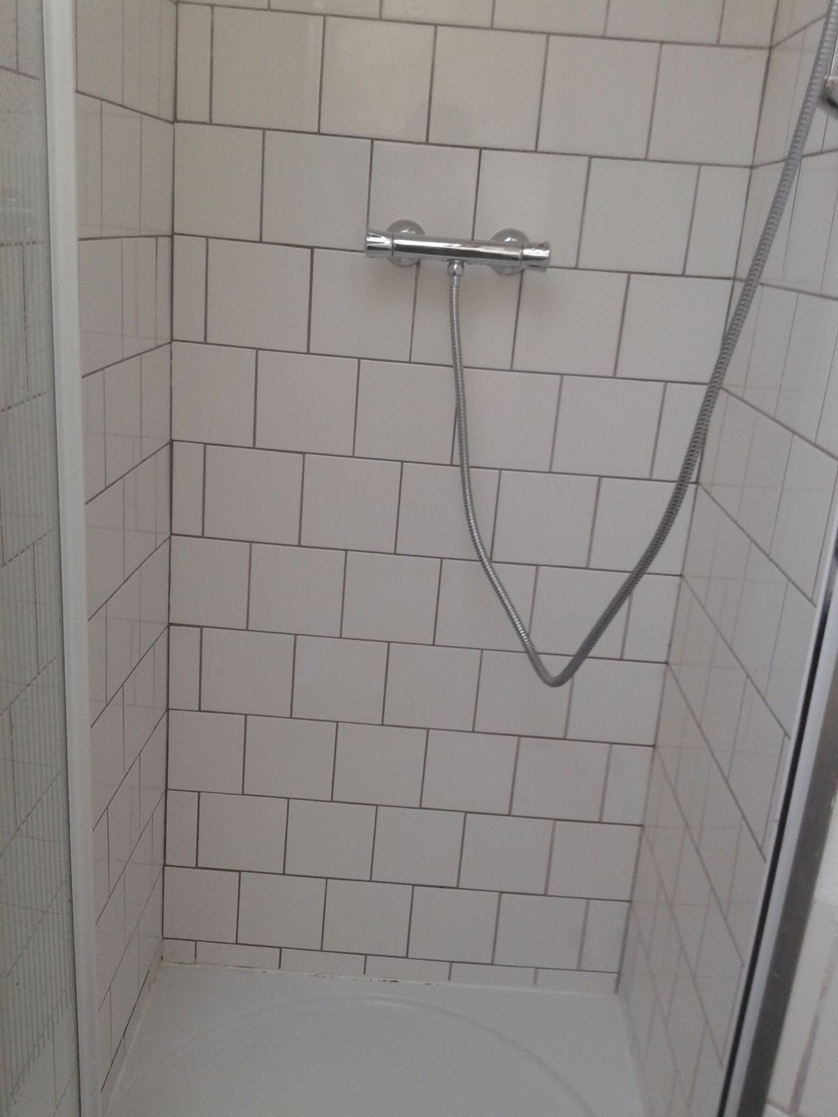 A shower with white tiles and a chrome showerhead.