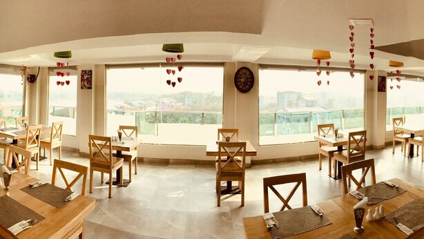 Un comedor amplio con varias mesas y sillas, ventanas grandes con vistas a la ciudad y una zona de bar con refrigerador.