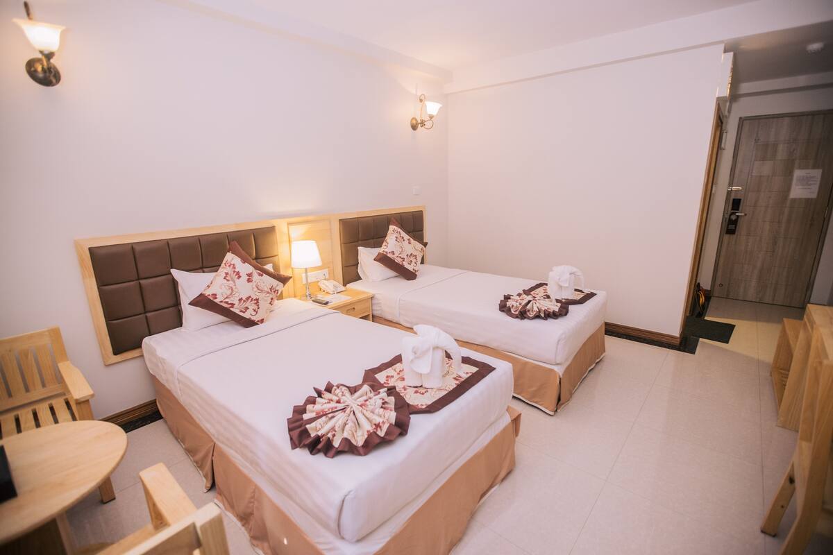 Una habitación de hotel con dos camas, una silla de madera, una mesita y una puerta.
