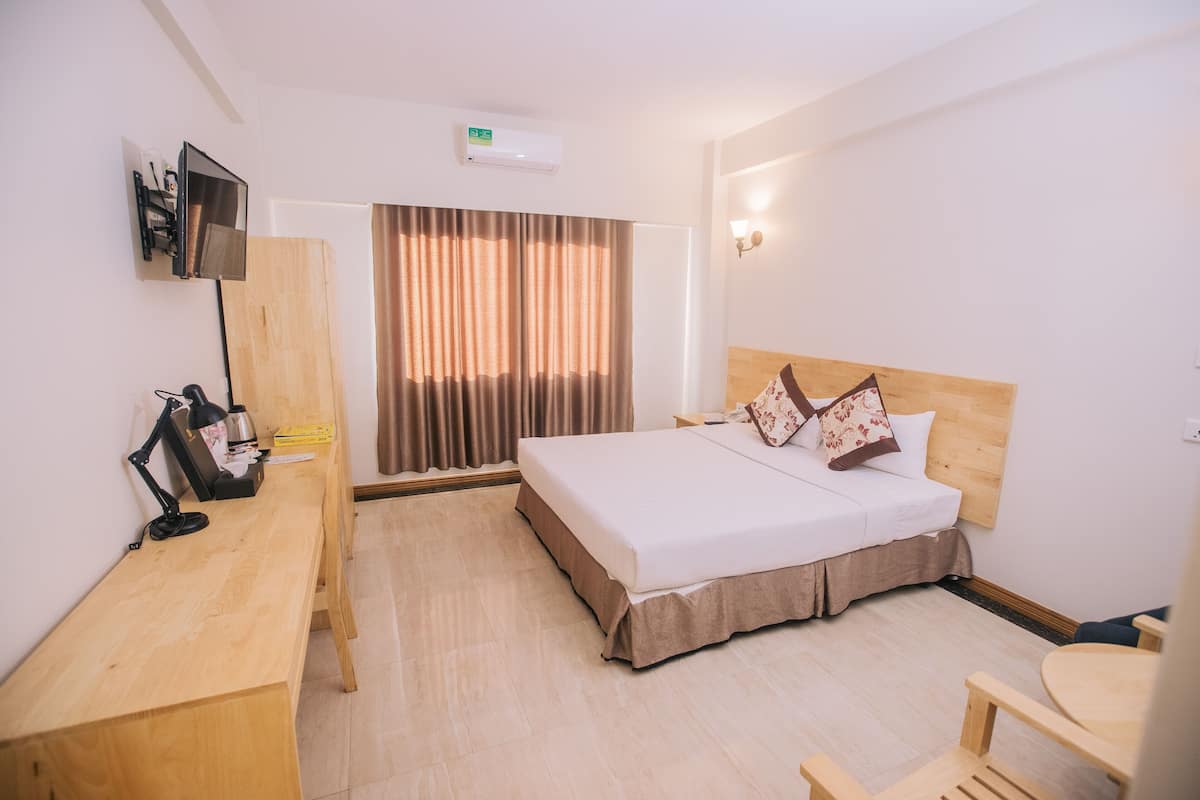 Habitación de hotel con cama, escritorio, silla y televisor montado en la pared.