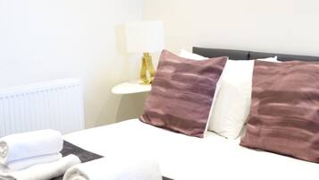 A hotel room with a neatly made bed, a bedside table with a lamp, and a radiator.