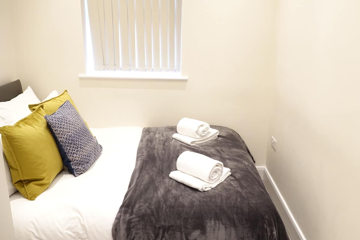 A neatly made bed with two rolled towels, a gray and white patterned pillow, and a yellow pillow.