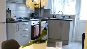 A modern kitchen with white cabinets, a dining table set for two, and a potted orchid. - The Close Airport (Hayes)