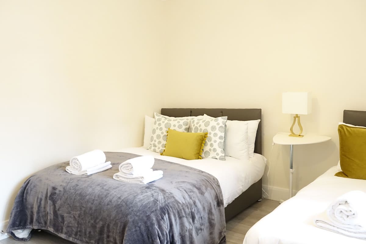A hotel room with two beds, a bedside table with a lamp, and towels on the beds.