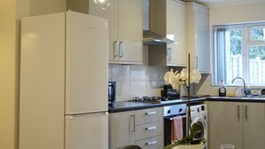 A modern kitchen with white cabinets, a refrigerator, a stove, and a dining table set for two with chairs. - The Close Airport (Hayes)