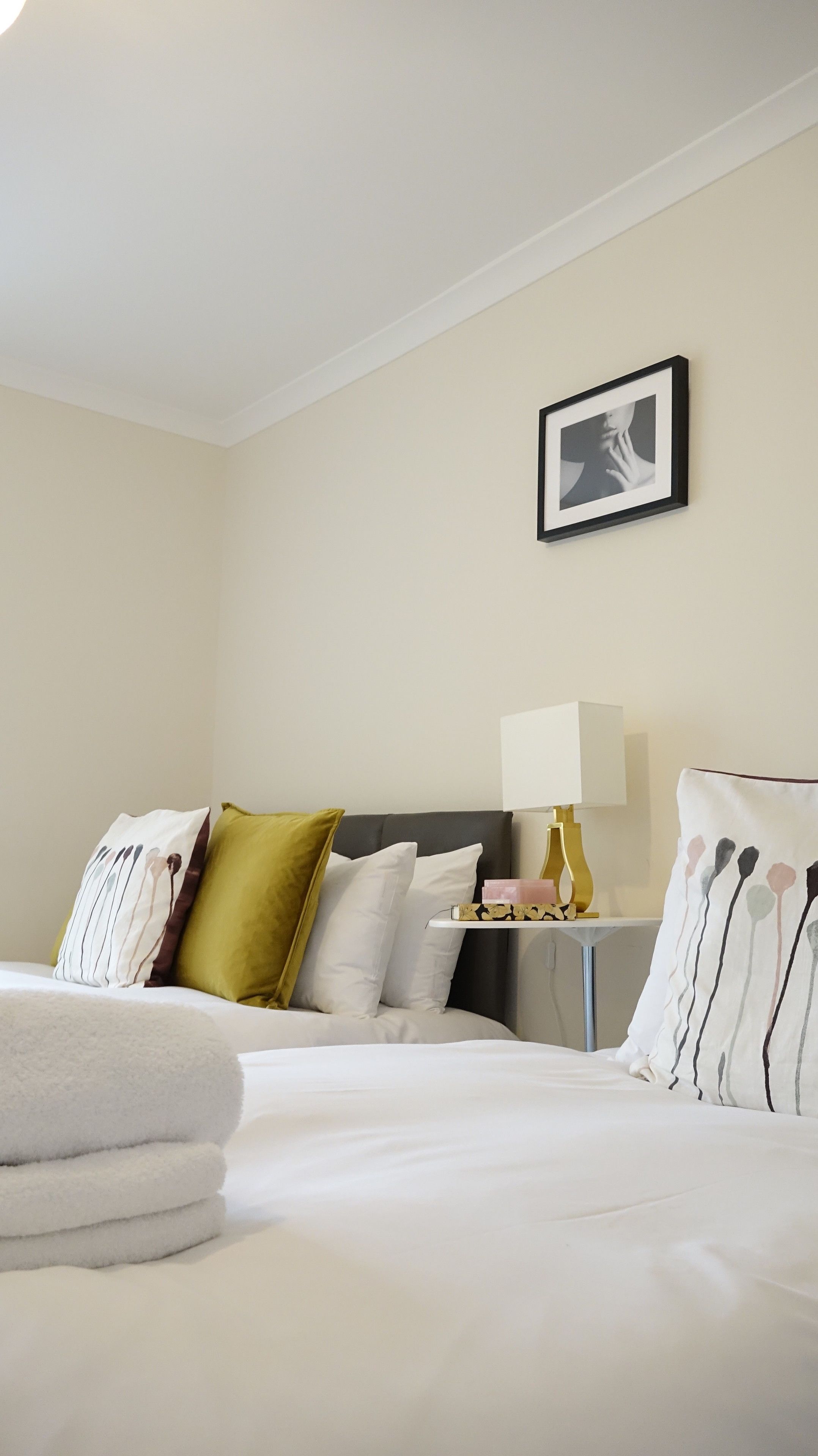 Quarto de hotel com cama bem arrumada, mesa de cabeceira com abajur e quadro na parede.