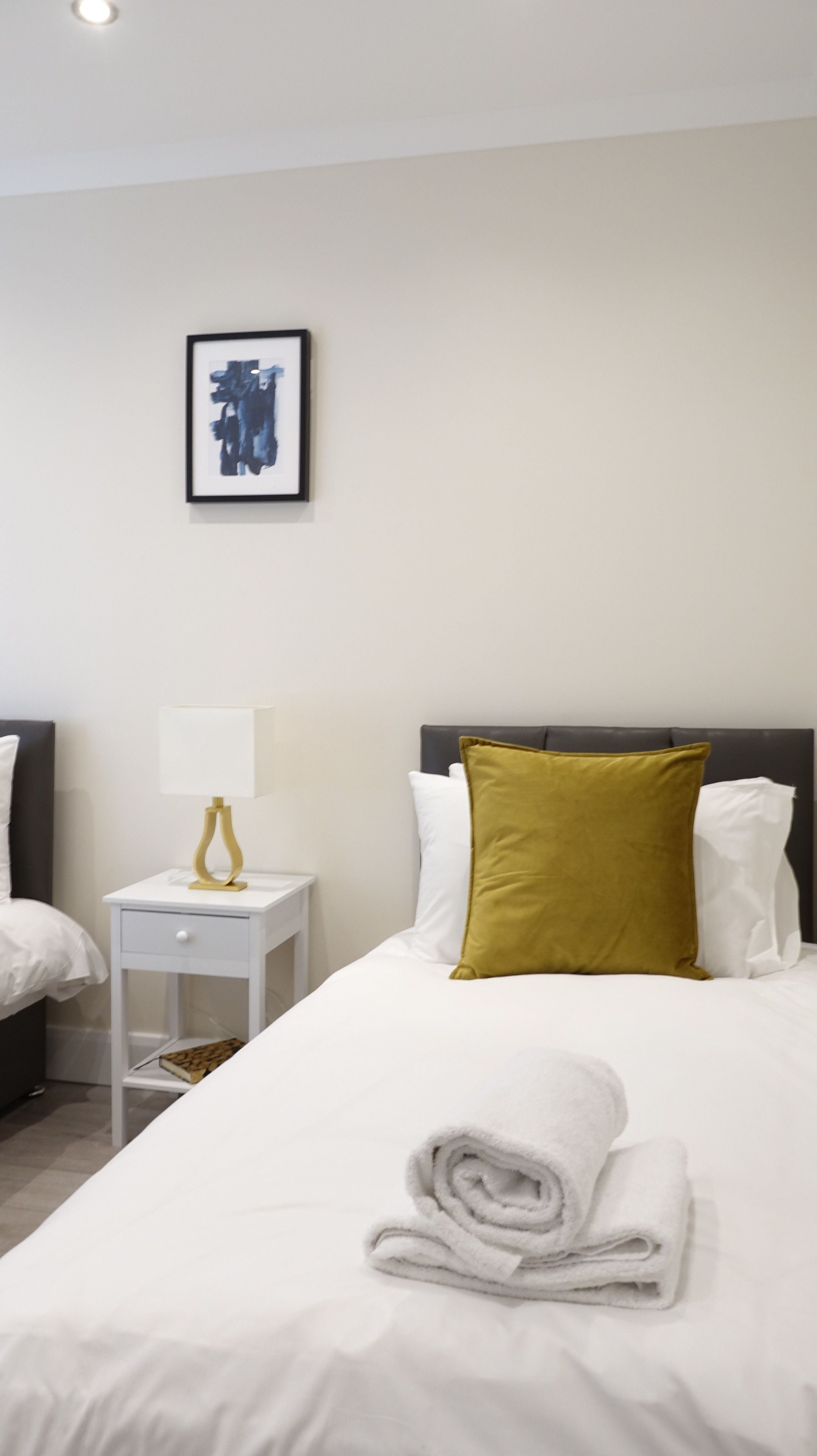 A hotel room with a neatly made bed, a bedside table with a lamp, and a framed artwork on the wall.