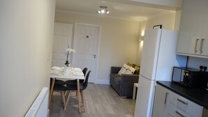 A compact kitchen with white cabinets, a refrigerator, and a dining area with a table and chairs. - The Close Airport (Hayes)