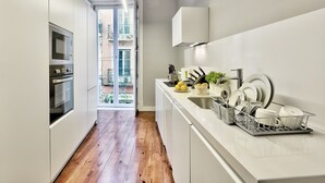 Une cuisine étroite avec des meubles blancs, un four encastré et une vue sur un balcon extérieur.