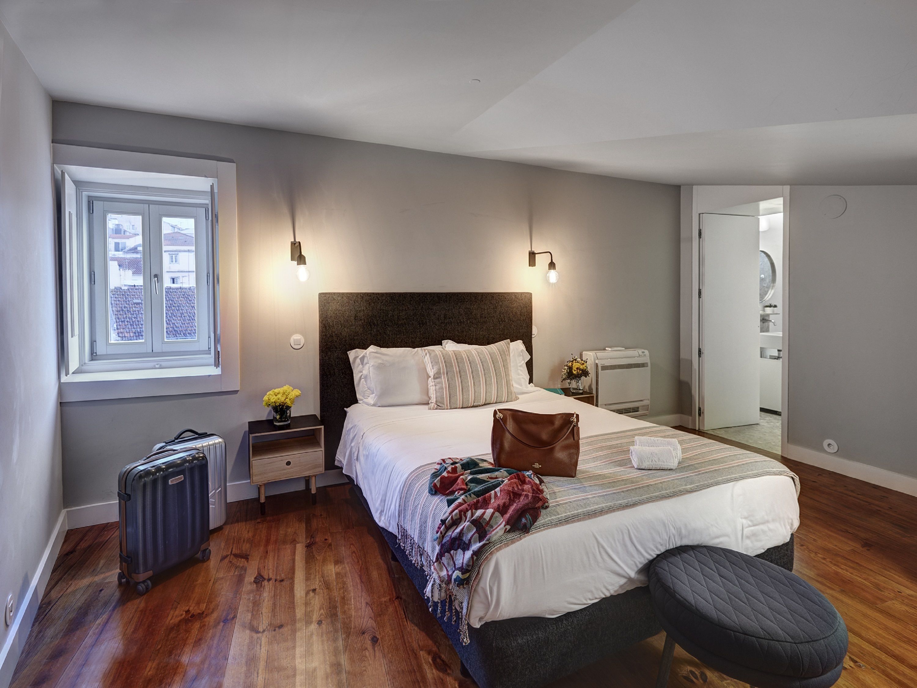 A bedroom with a large bed, bedside tables, a suitcase, and a window.