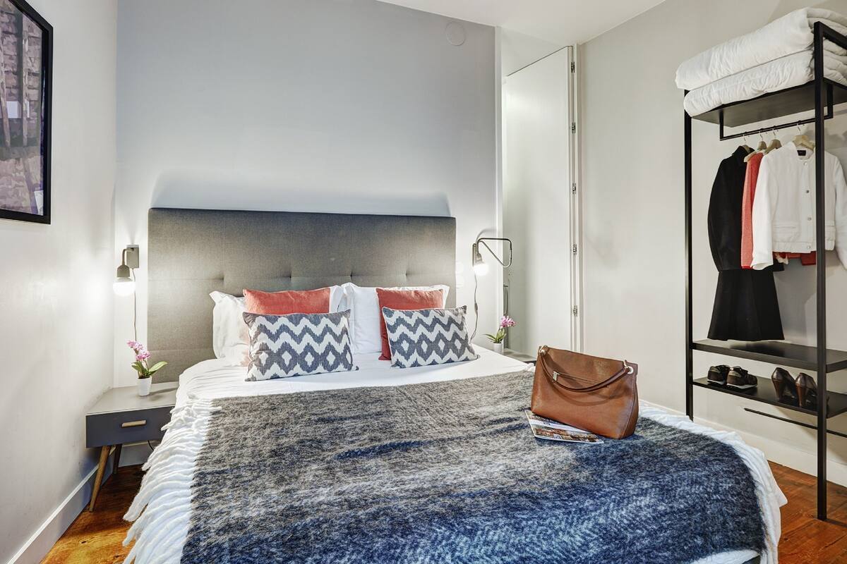 A modern hotel room with a large bed, a bedside table, a wardrobe, and a mirror.
