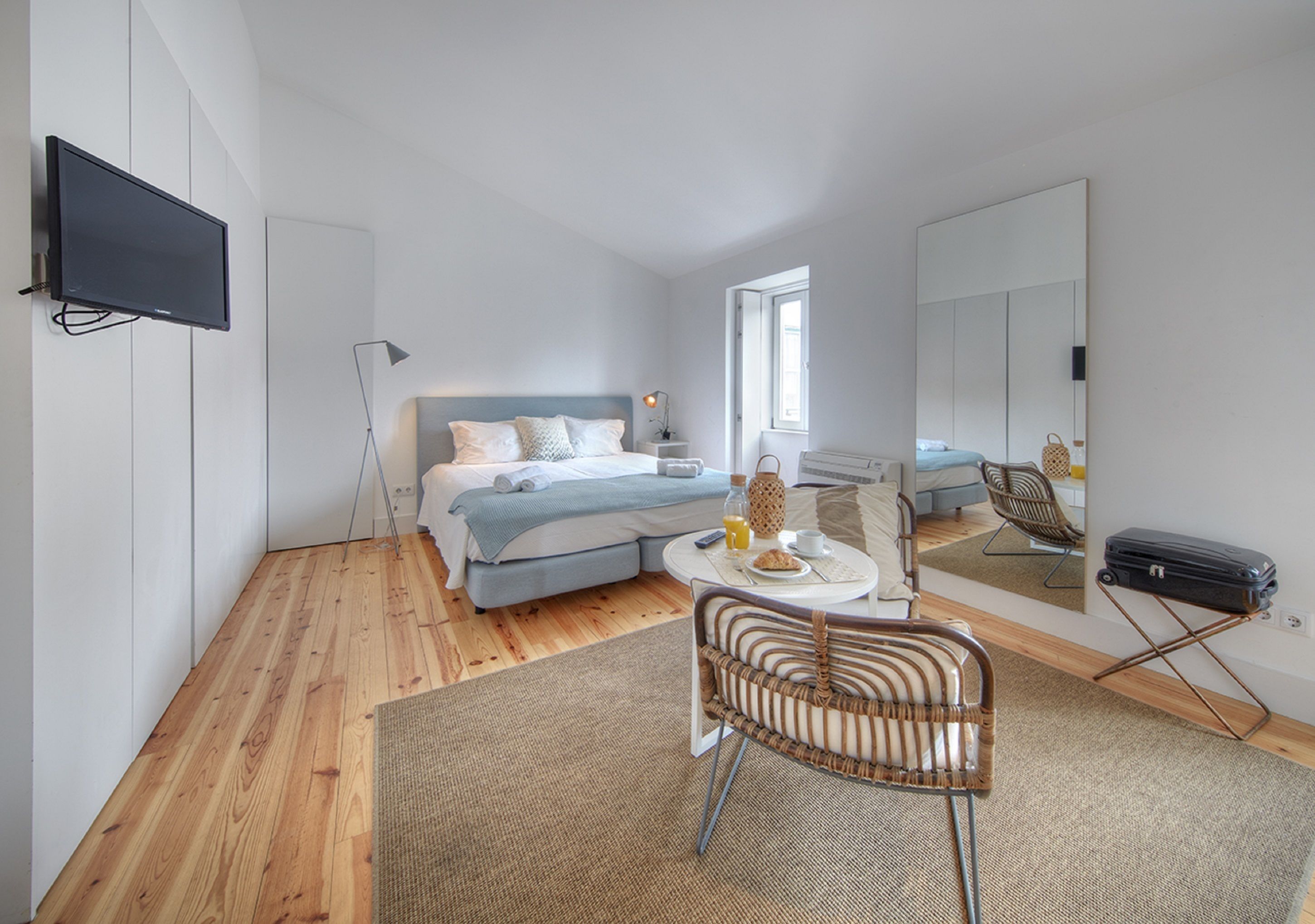 A modern bedroom with a bed, bedside table, lamp, chair, and a suitcase.