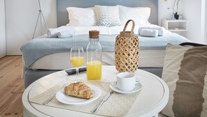 Une table de petit-déjeuner soigneusement dressée, avec des croissants, du jus de fruits et une tasse, dans une chambre d’hôtel moderne. On aperçoit un lit et des lampes de chevet à l’arrière-plan.