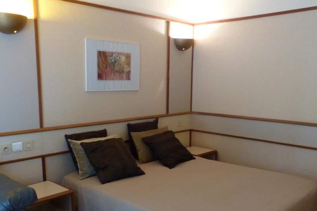 Une petite chambre à coucher, bien rangée, avec un lit simple, une table de chevet et une chaise.