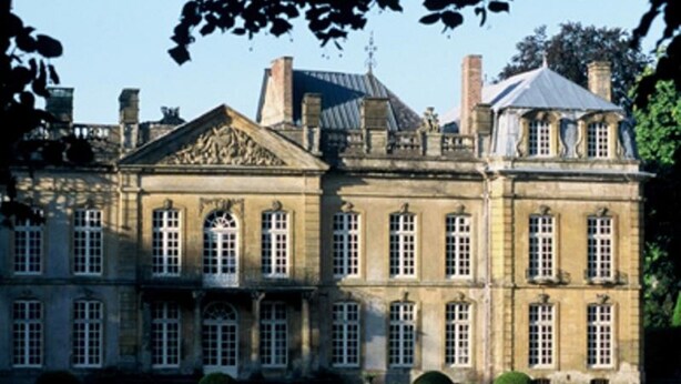 Een groot, historisch pand met symmetrische architectuur, veel ramen en een verzorgd gazon.