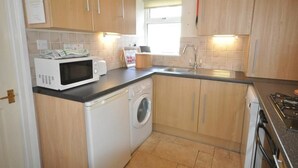 A compact kitchen with wooden cabinets, a microwave, a washing machine, and a sink. - Green Door Rose (Port Isaac)