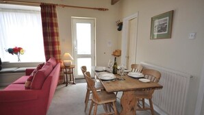 A dining area with a wooden table set for four, a red sofa, and a window with curtains. - Green Door Rose (Port Isaac)