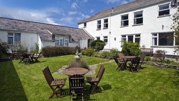 A well-maintained garden with a wooden table and chairs, surrounded by white buildings with multiple windows. - Green Door Rose (Port Isaac)
